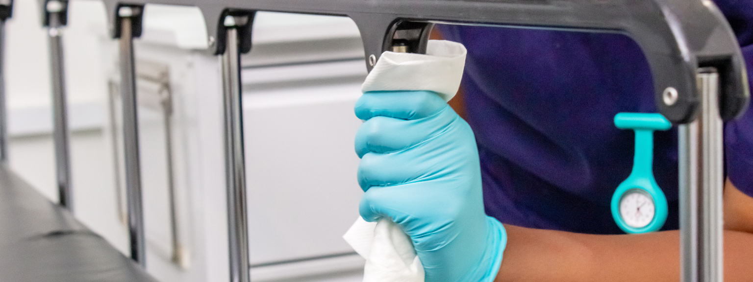 Hand van een zorgverlener met handschoen op een ziekenhuisbedhek