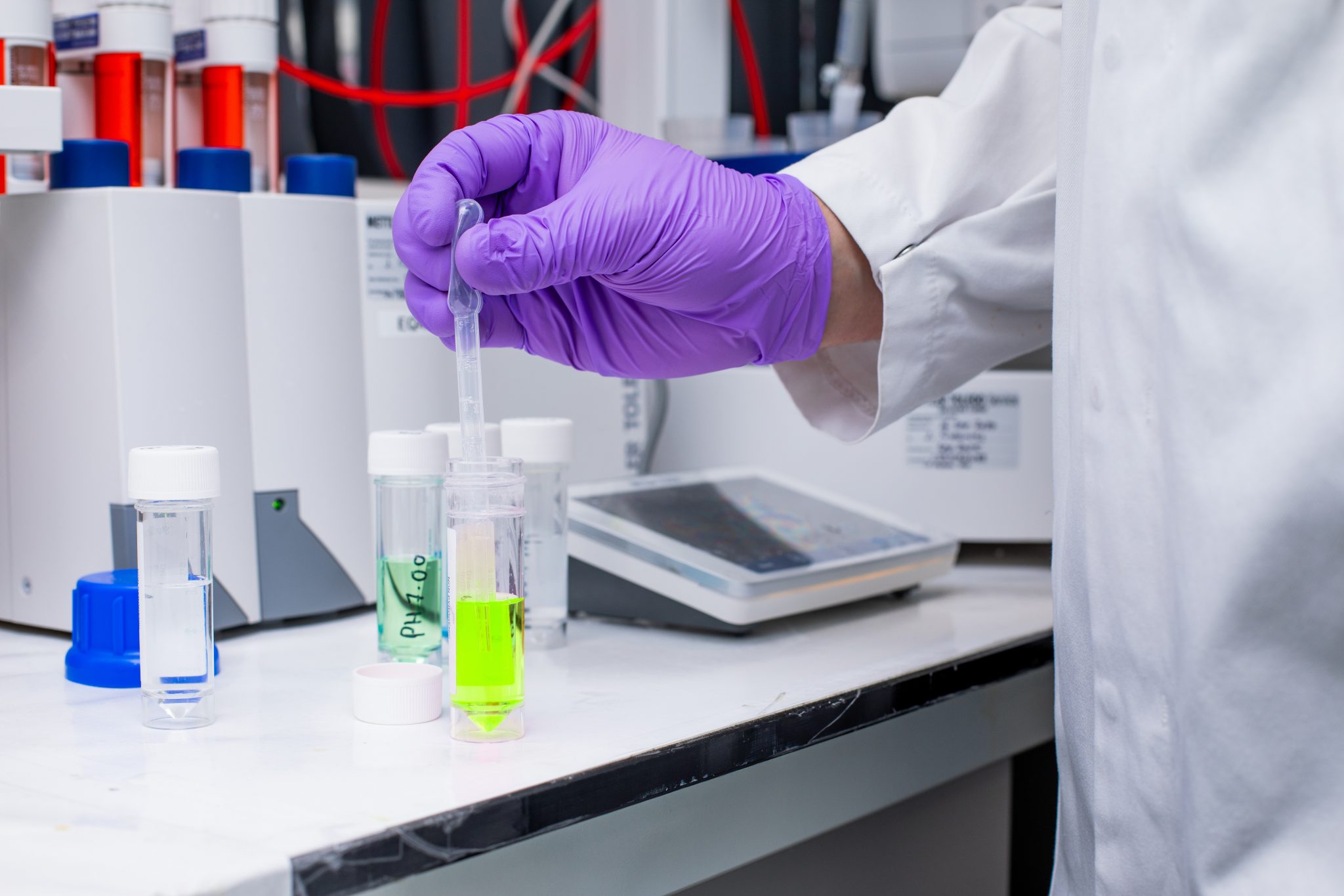 Scientist in purple gloves using a pipette with a green solution in a laboratory